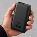 A hand holding the GOBI 6500-PD battery, with the USB-A and USB-C ports, charge indicator lights, and side power button visible.