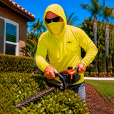Man in a hi-vis yellow GOBI Helio UPF Sun Hoodie trimming hedges with a gas-powered hedge trimmer in a residential landscape with palm trees in the background.