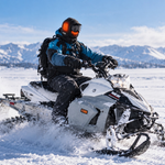 Snowmobile rider wearing the black GOBI Squall heated balaclava in a snowy mountain setting.