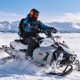 Snowmobile rider wearing the black GOBI Squall heated balaclava in a snowy mountain setting.