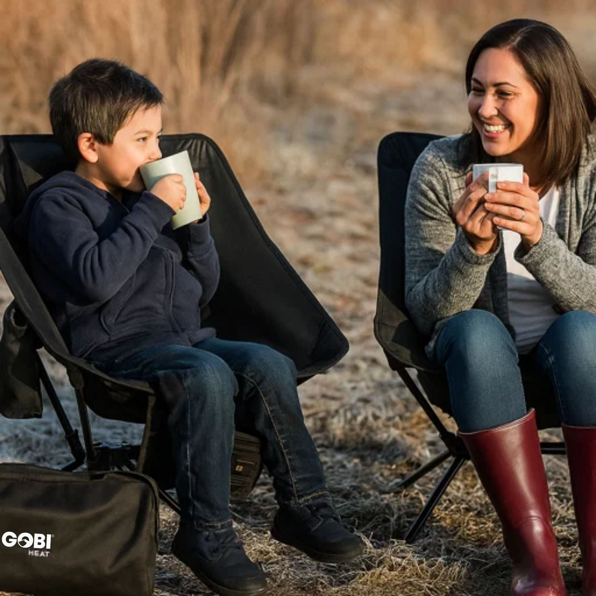 Woman and child sitting in Beck Ultra-Portable Heated Camping Chairs drinking from mugs outdoors